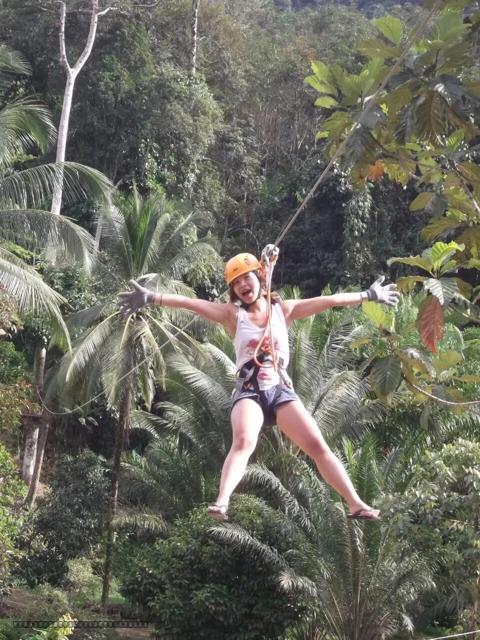 Tourist soaring on the Flying Fox zipline over the river in the Phang Nga tropical forest.